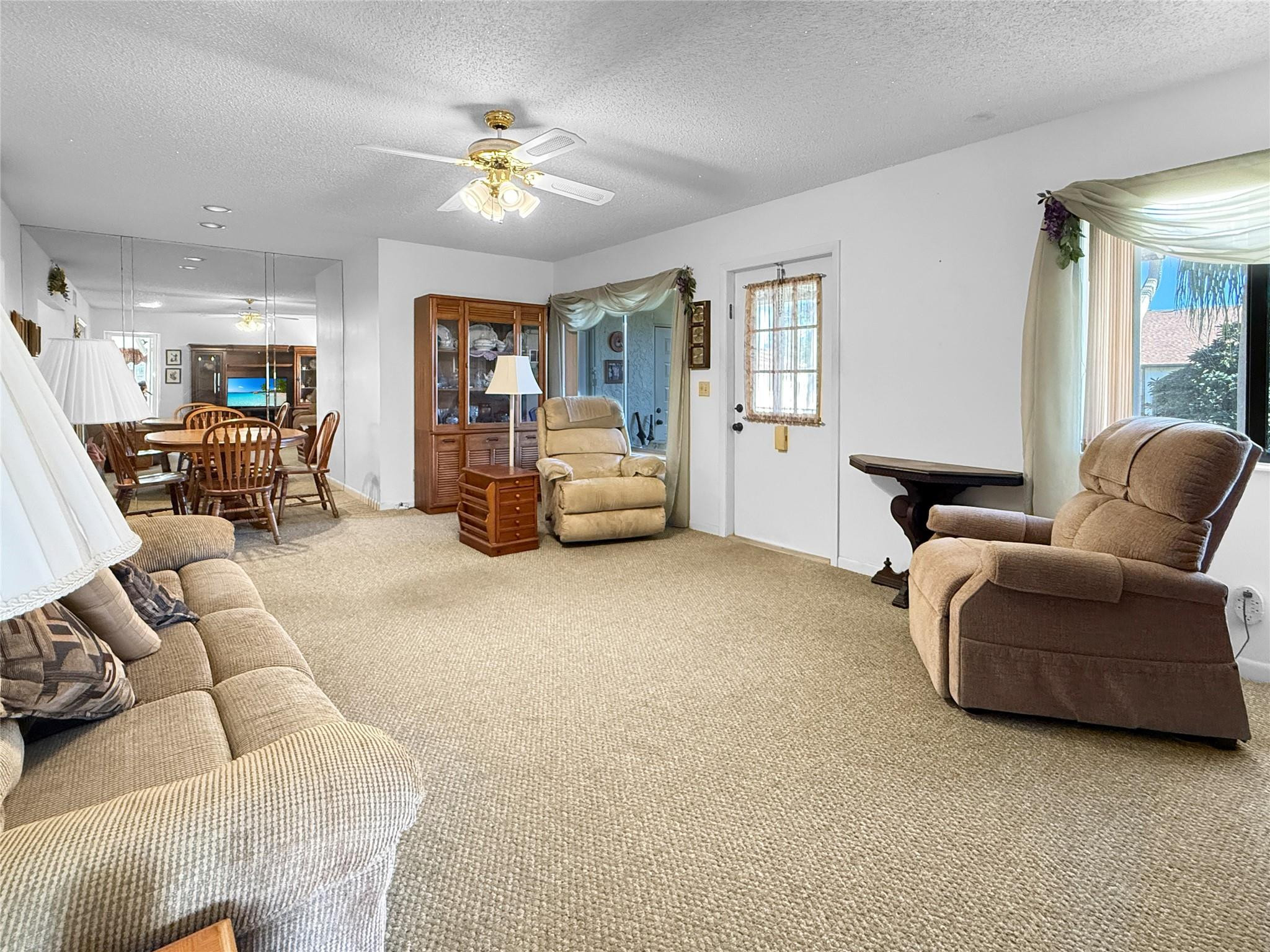 Furnished living room with beige carpet, recliners, mirrored wall, and dining area.
