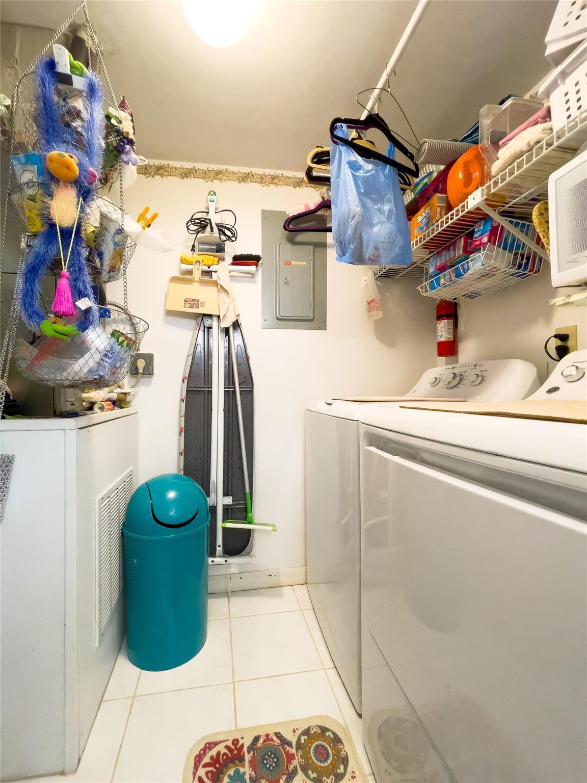 Laundry room with a washer and dryer, overhead wire shelves, and ironing boards stored against the wall.