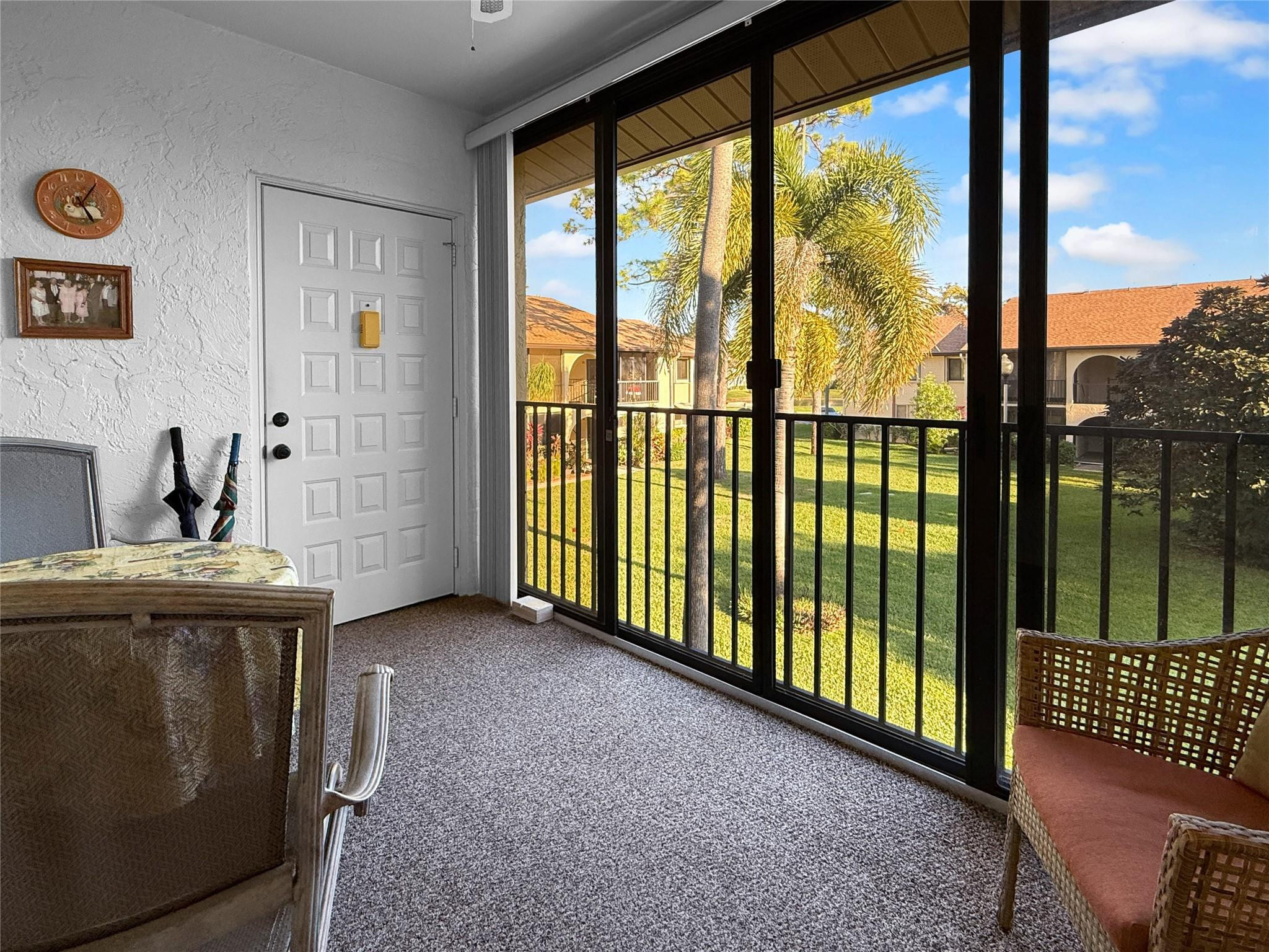 Carpeted sunroom with sliding glass doors overlooking a palm-lined courtyard.