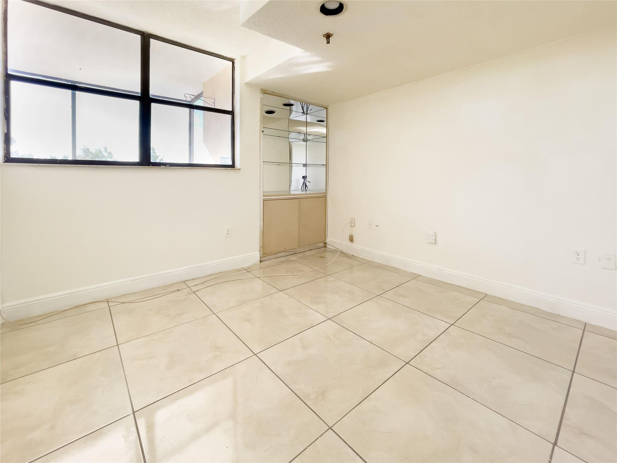 Empty room with cream tile floors, a large black-framed window, and mirrored built-in cabinet.