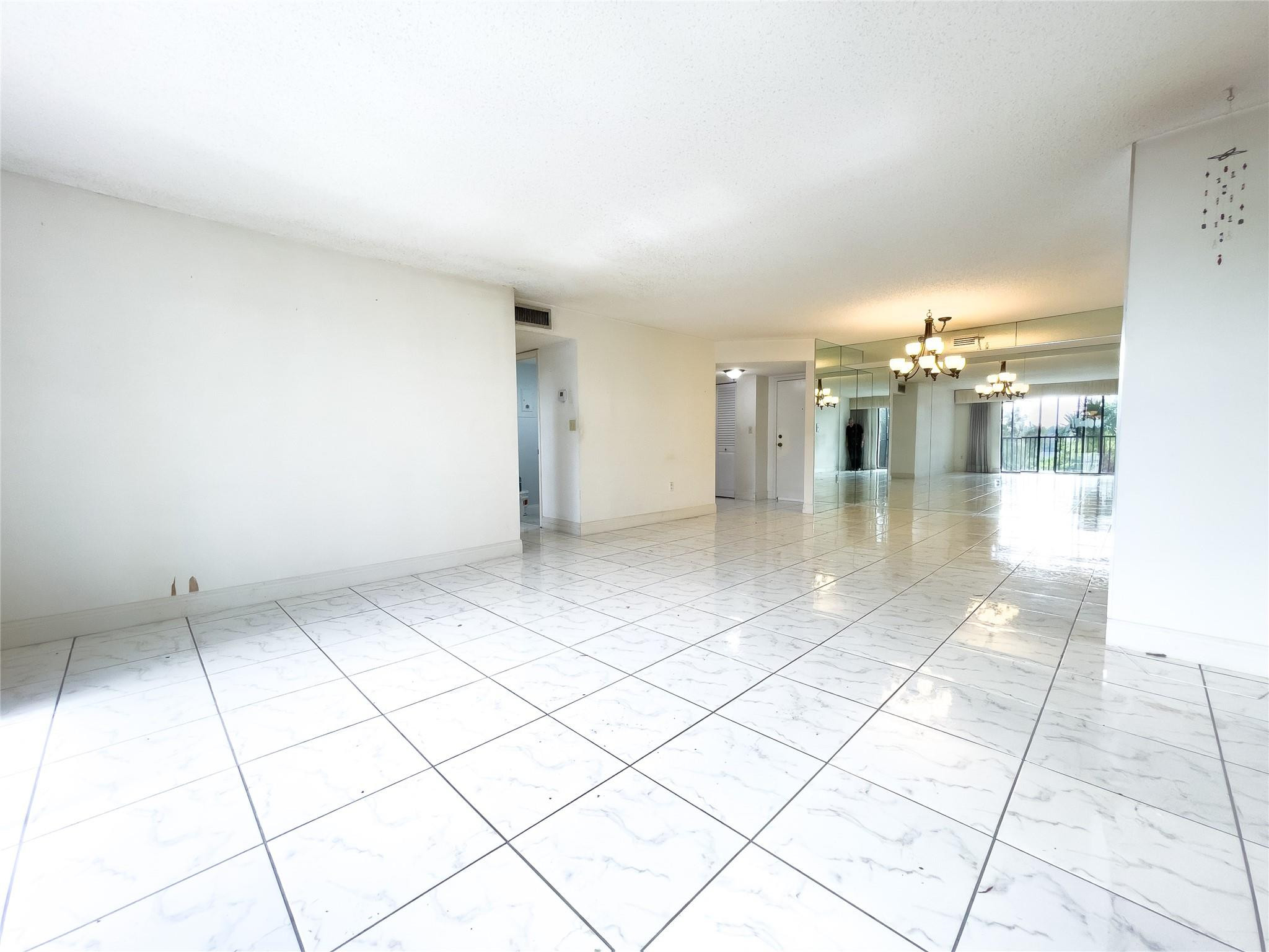 Vacant condo living area with glossy tile, mirrored walls, chandelier, and balcony doors.