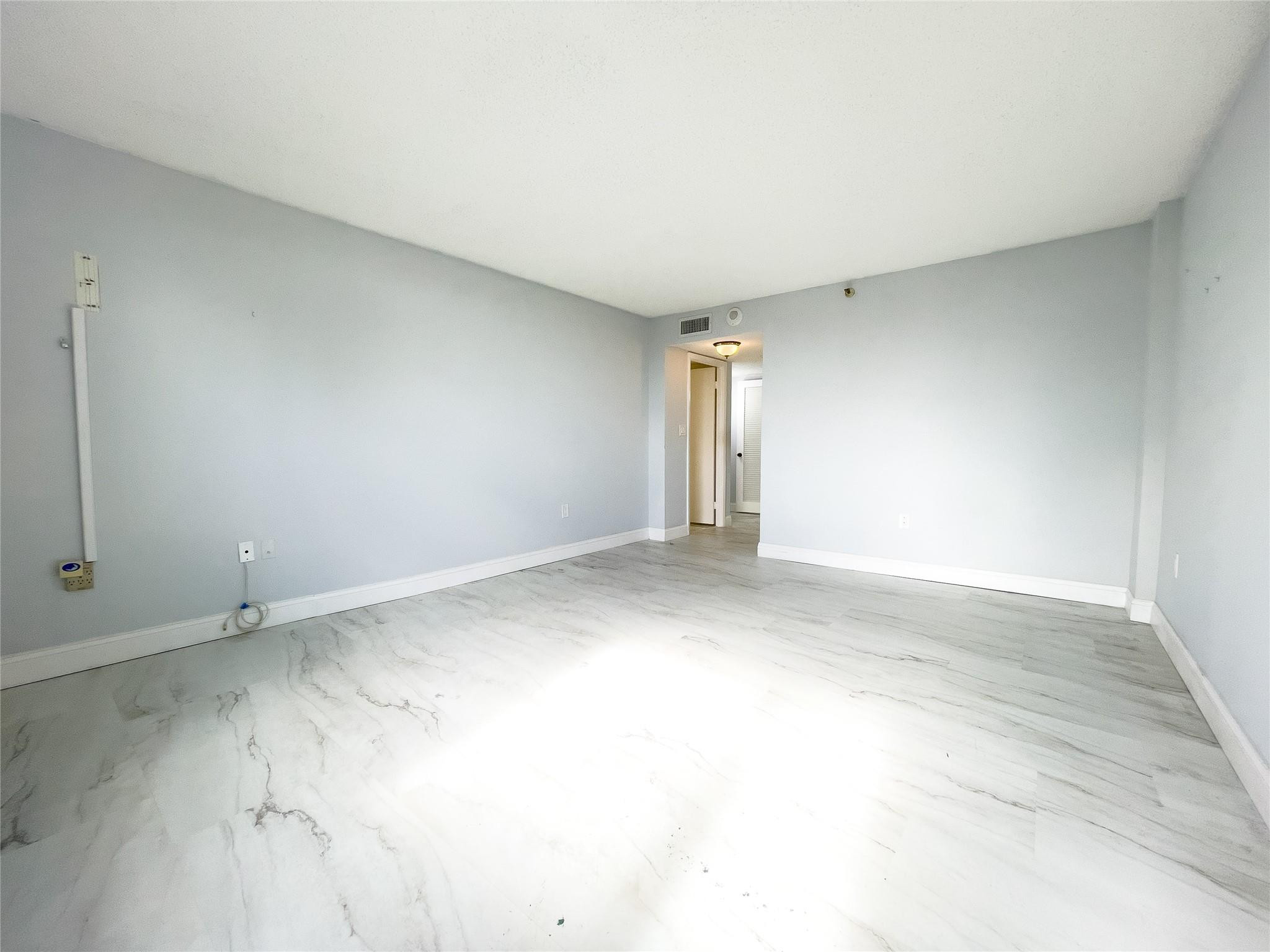 Empty room with pale gray walls, marble-pattern flooring, and an open doorway