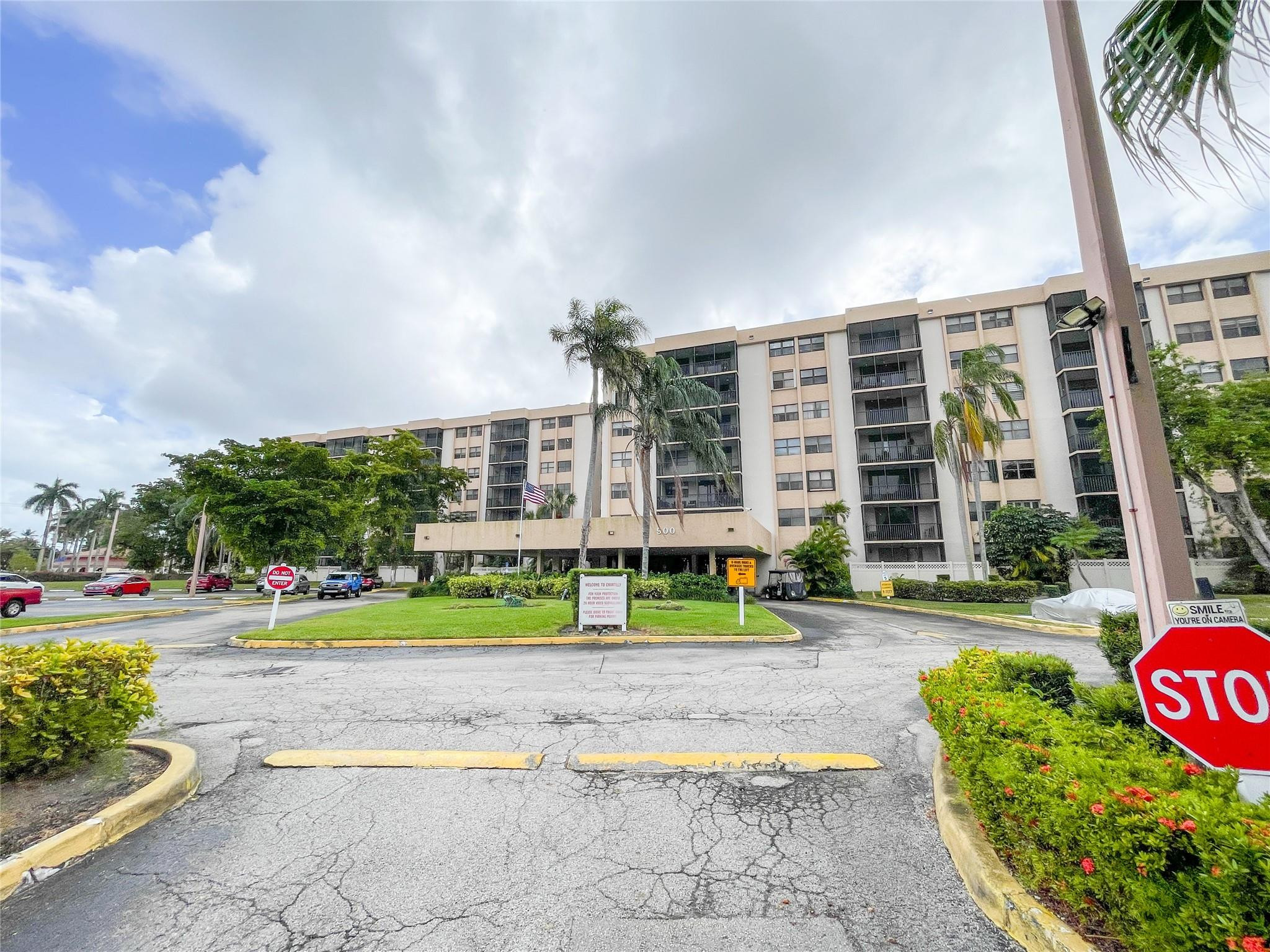 Condominium building at 900 NE 195th St, with a landscaped entrance drive and palm trees.