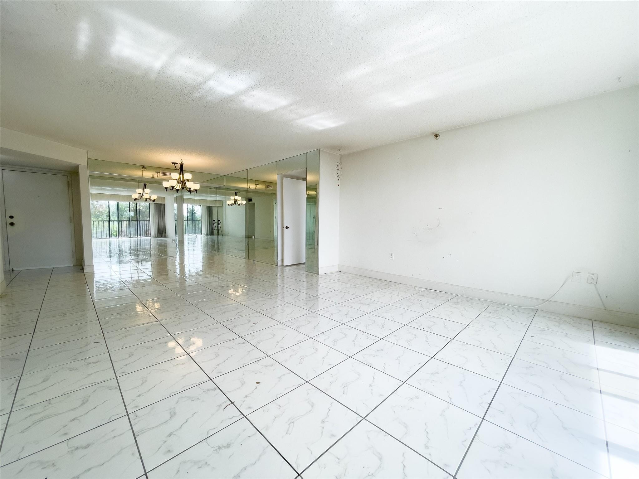Vacant living room with glossy tile floors, mirrored wall, chandelier, and balcony doors.