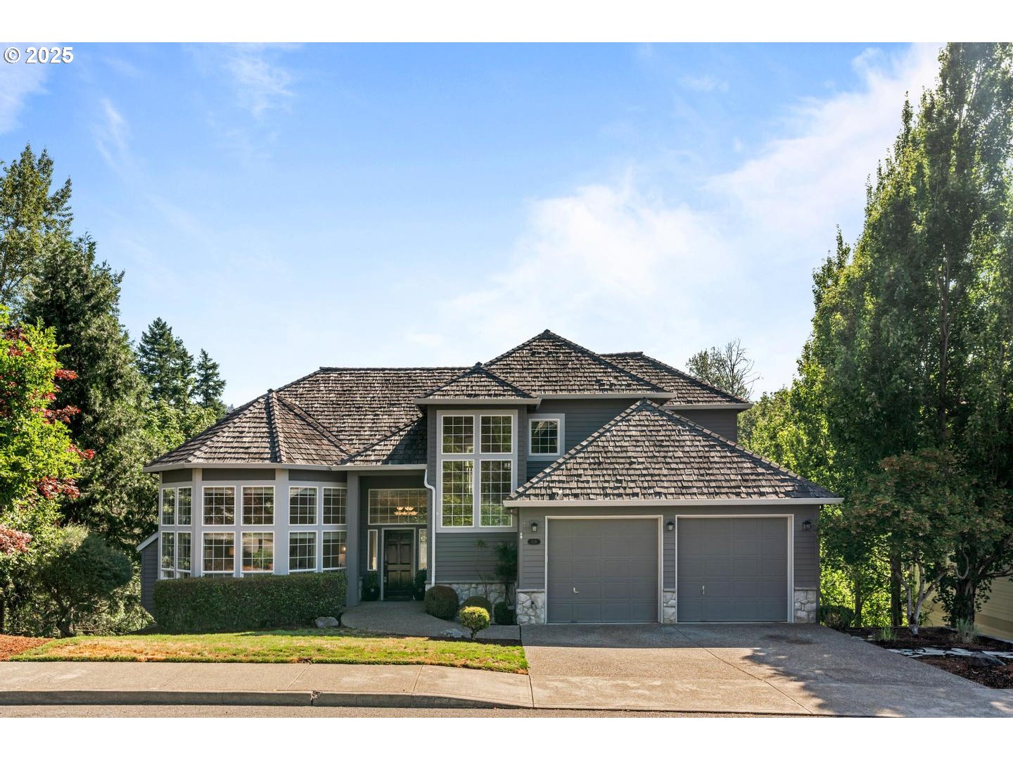 Gray two-story house with a shingle roof, large windows, stone accents, and a two-car garage.
