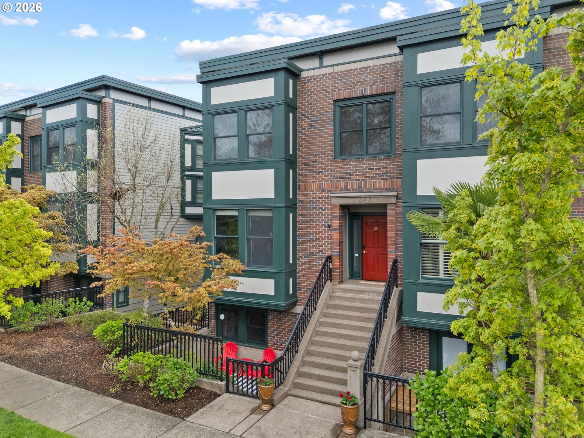 Brick residential building with dark green trim, a red entry door, and landscaped front steps.