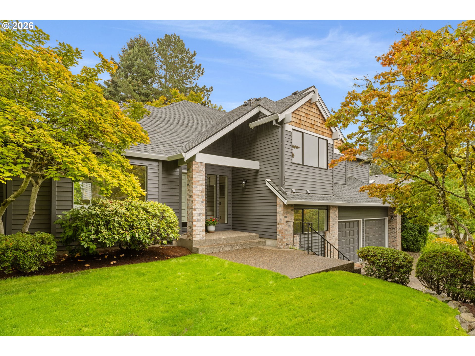 Gray two-story home with brick columns, a double garage, and autumn trees framing the lawn.