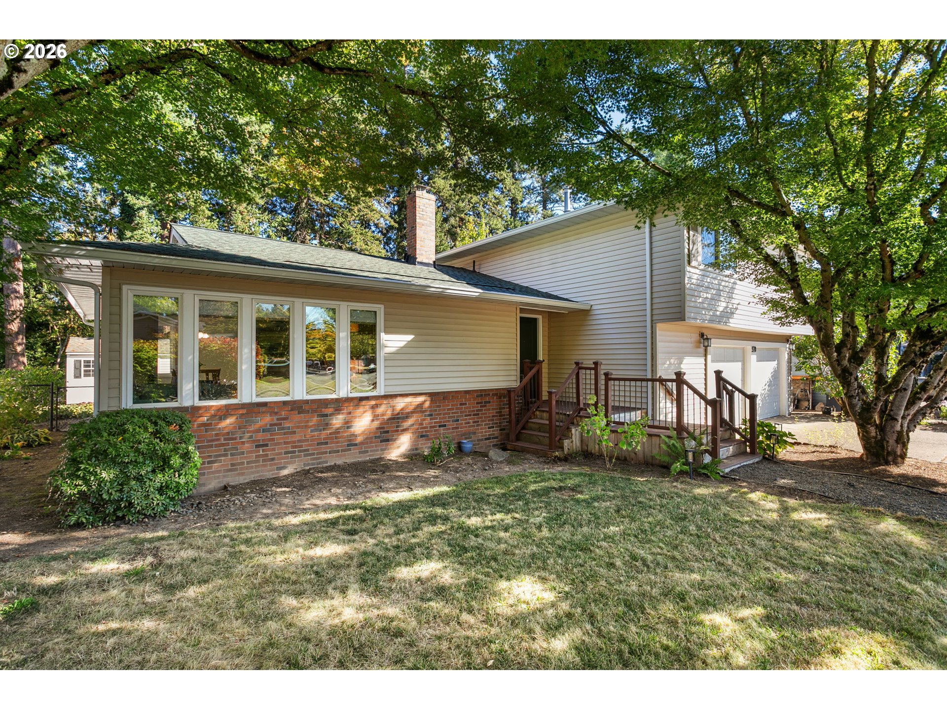 House exterior with brick lower walls, raised deck, garage, and mature shade trees.