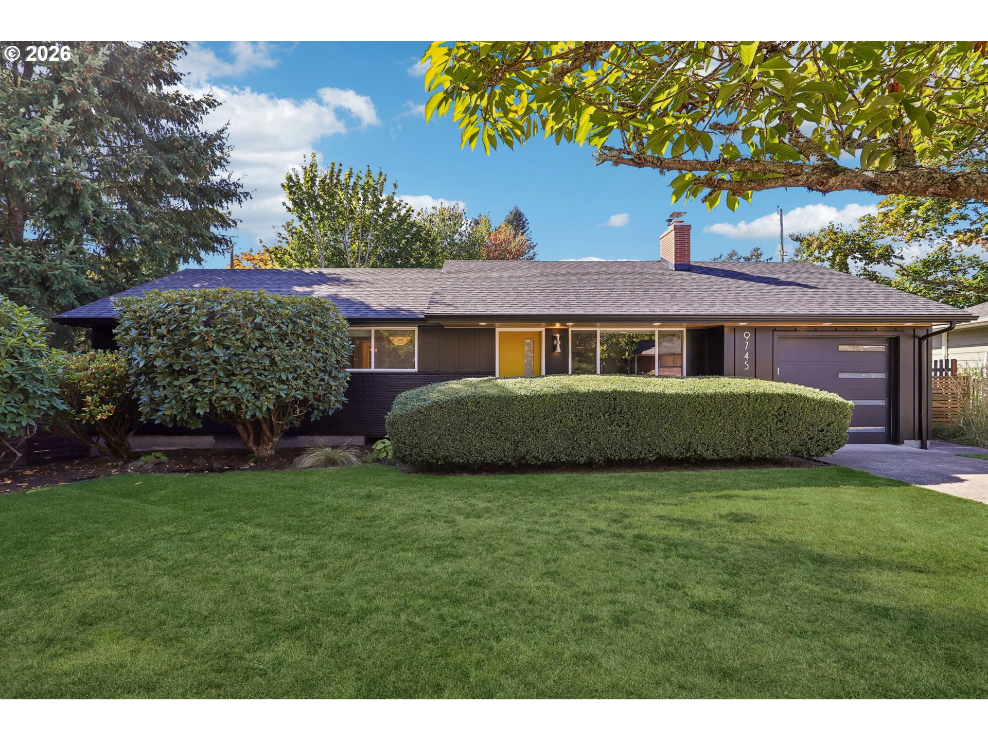 Single-story ranch house with a yellow front door, dark siding, and manicured lawn.