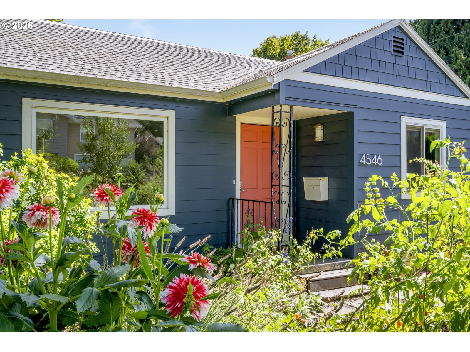 Blue house with a coral-red front door and dahlias blooming in the front garden.