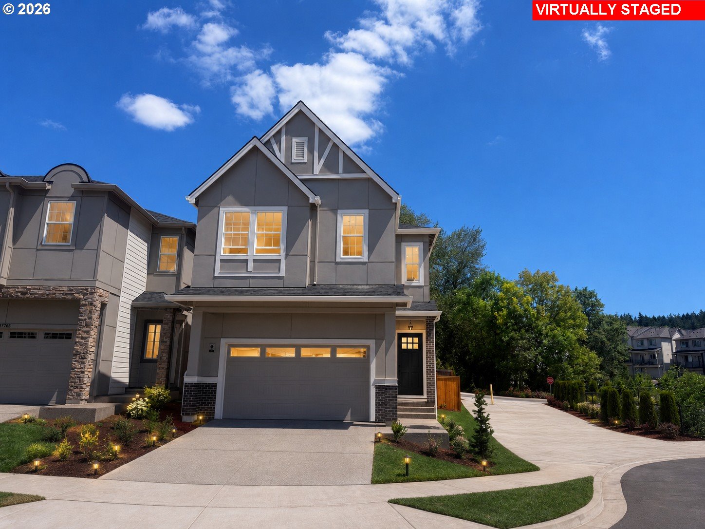 Gray multi-story home with peaked gables, stone accents, a two-car garage, and landscaped front yard.