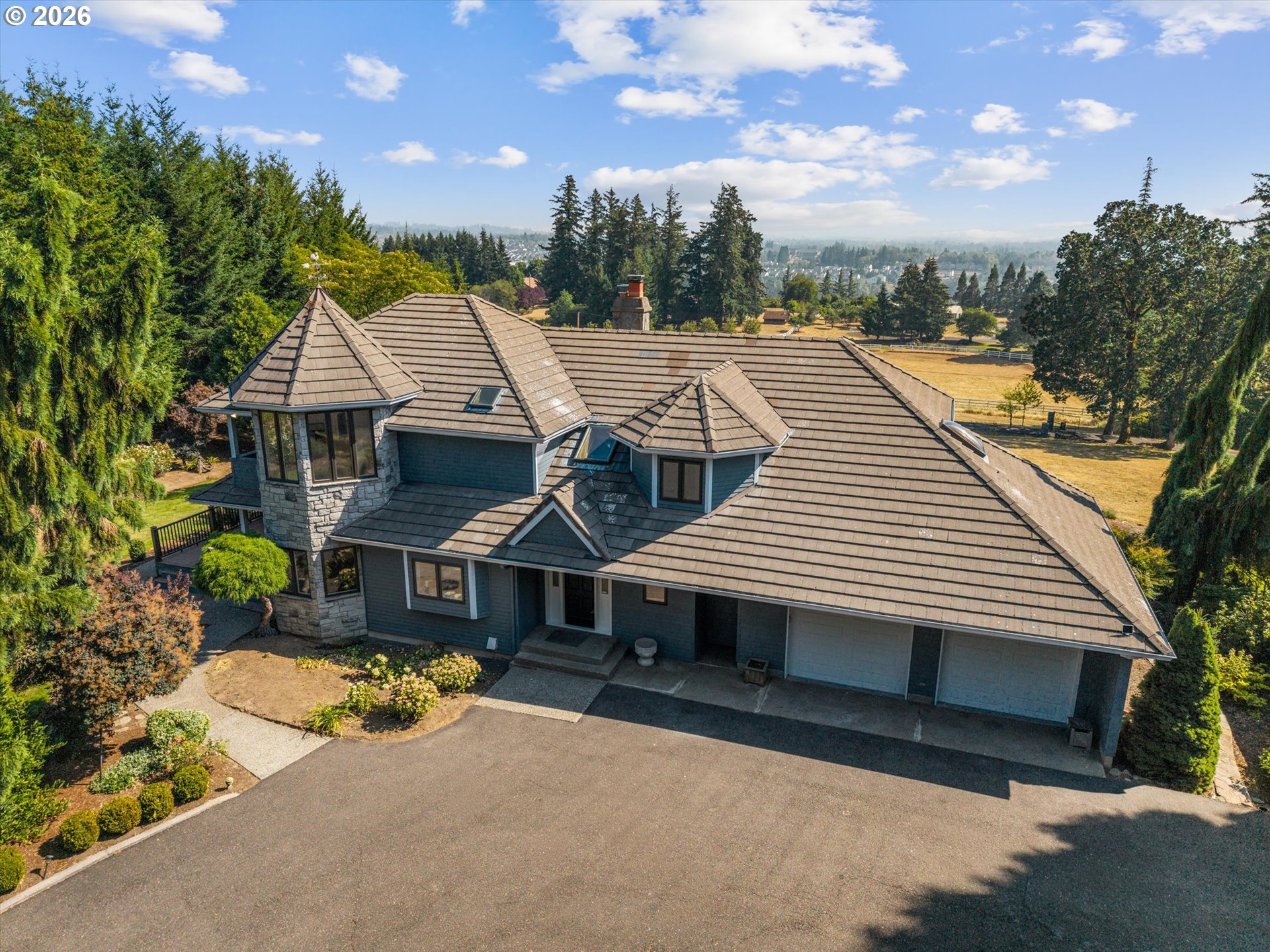 Aerial view of a stone-and-blue-gray home with a broad tiled roof and landscaped grounds.