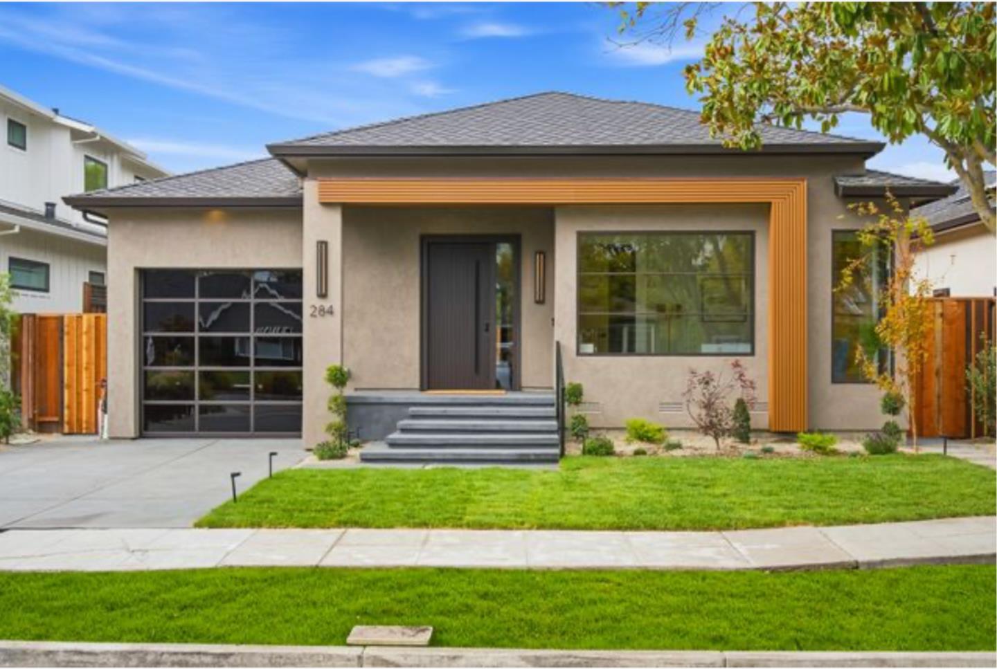 Modern single-story home with distinctive orange trim, a dark garage door, and a green front lawn.