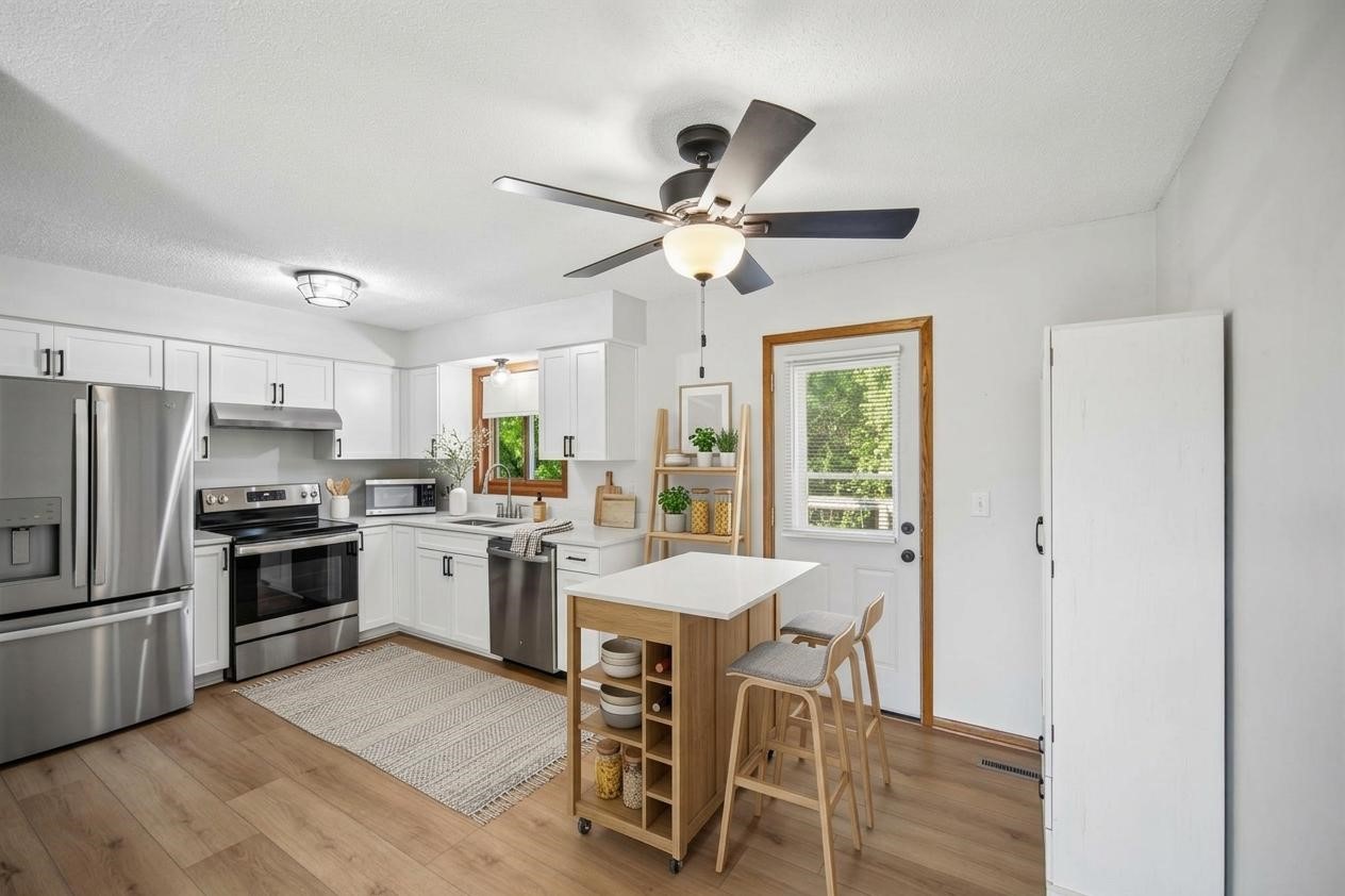 Bright kitchen with white cabinets, stainless steel appliances, and a wood island with stools.