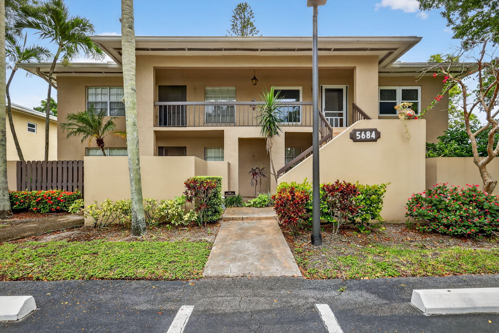 Beige two-story residence with balconies, exterior stairs, tropical landscaping, and a 5684 address plaque.