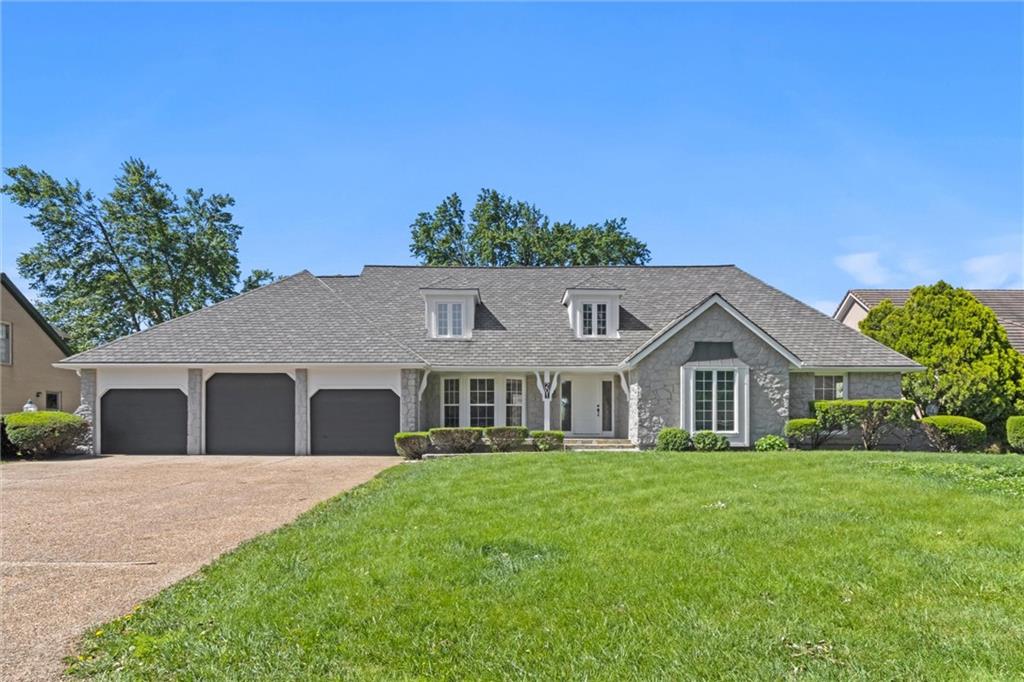 Gray stone home with a three-car garage, dormer windows, and a broad green lawn.