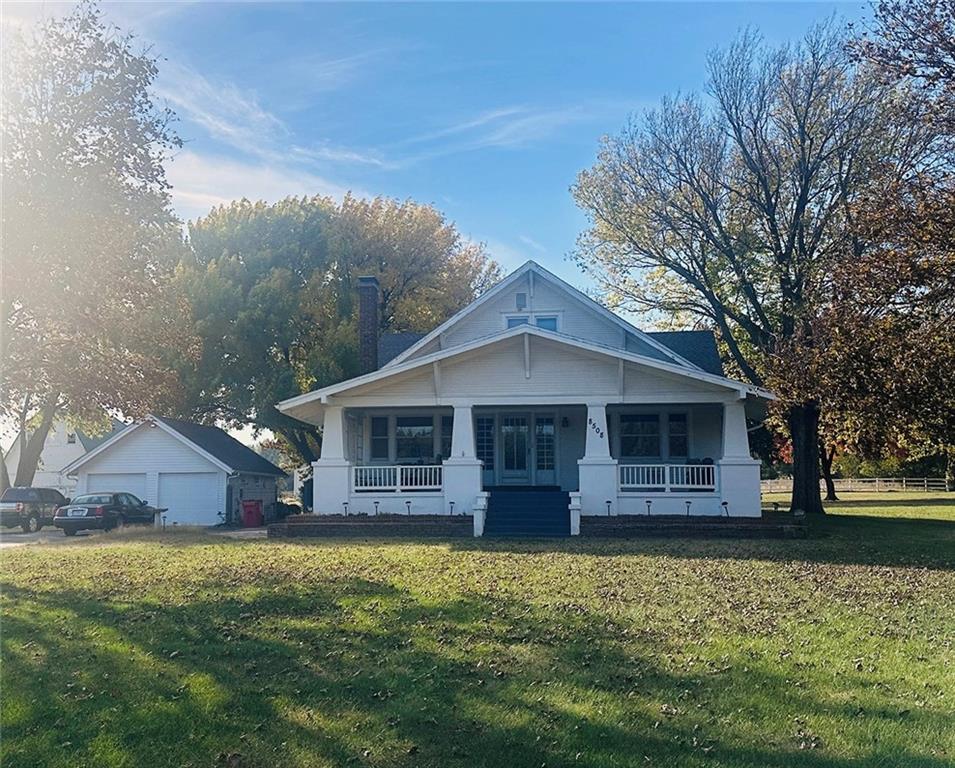 White bungalow with a broad covered porch, dark front steps, and detached garage beneath autumn trees.
