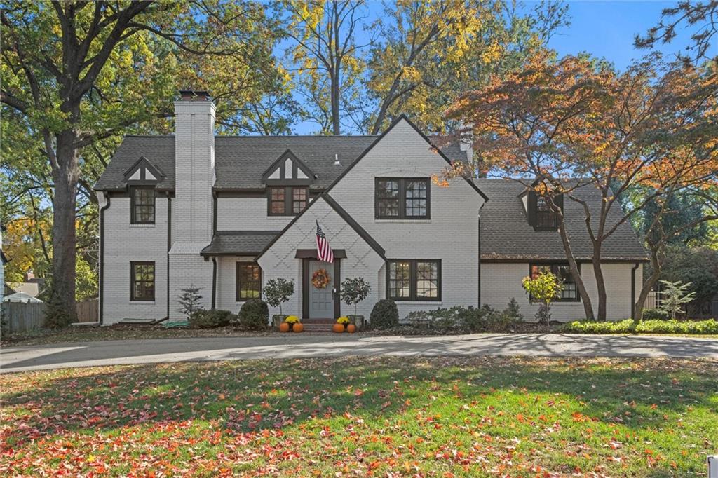 Two-story white brick house with a dark gabled roof, chimney, and pumpkins by the front entrance.