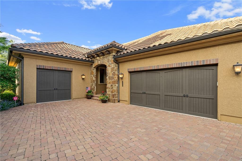 Home exterior with three dark garage doors, a stone entry, and a brick-paver driveway.