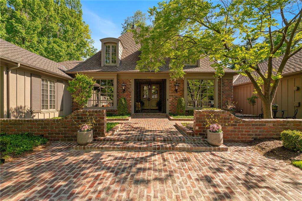 Home with a brick courtyard and walkway beneath mature trees.