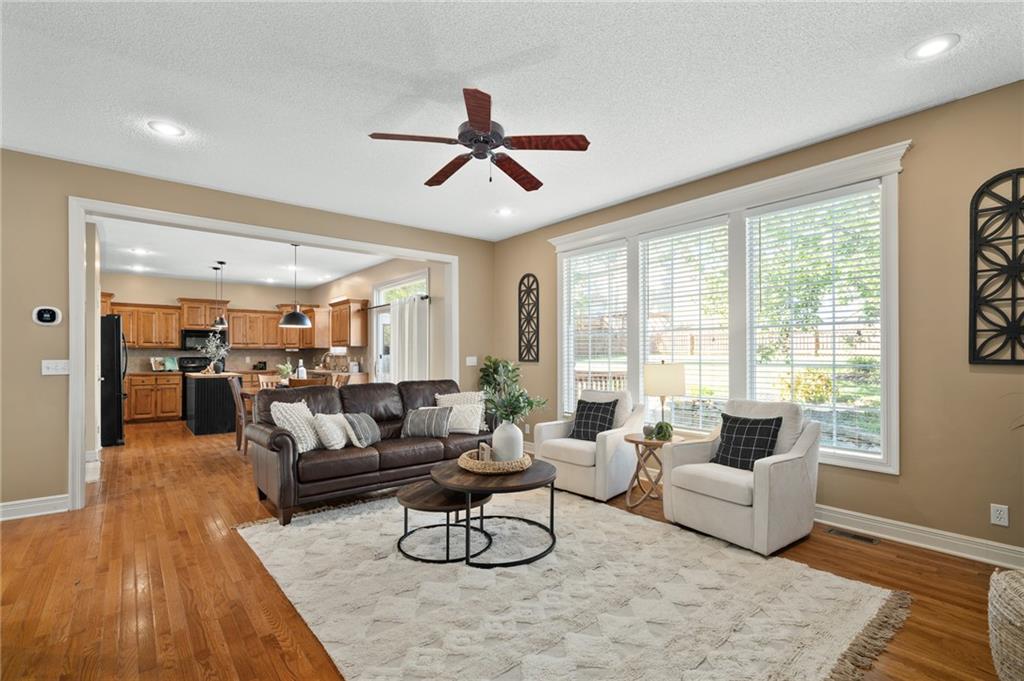 Open-plan living room with a leather sofa, white armchairs, hardwood floors, and large windows.
