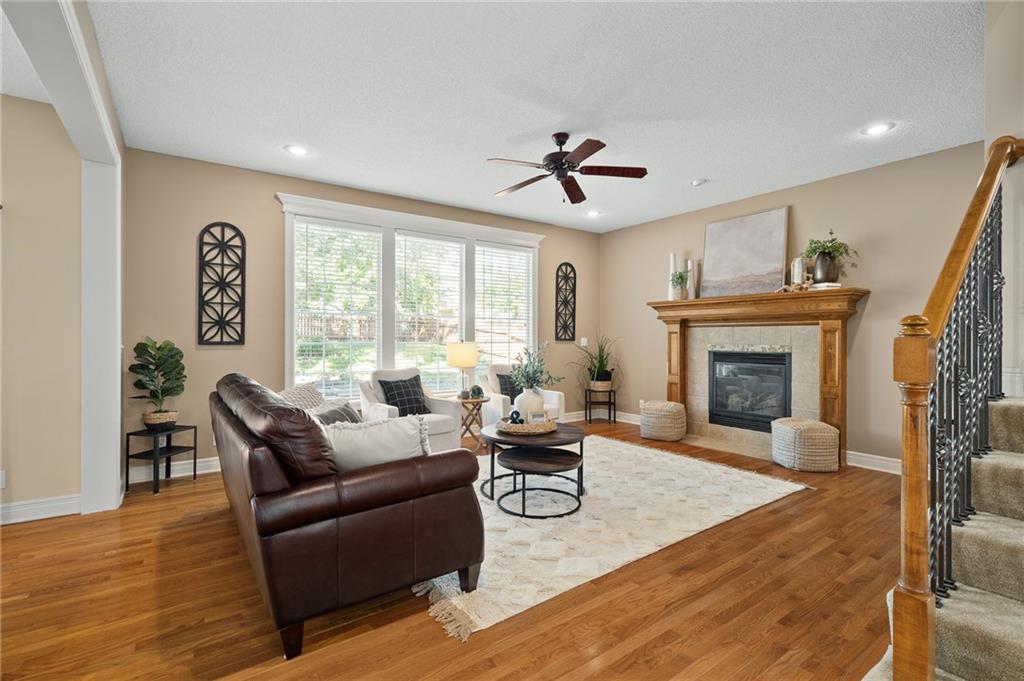Living room with a stone fireplace, large windows, hardwood floors, and a carpeted staircase.