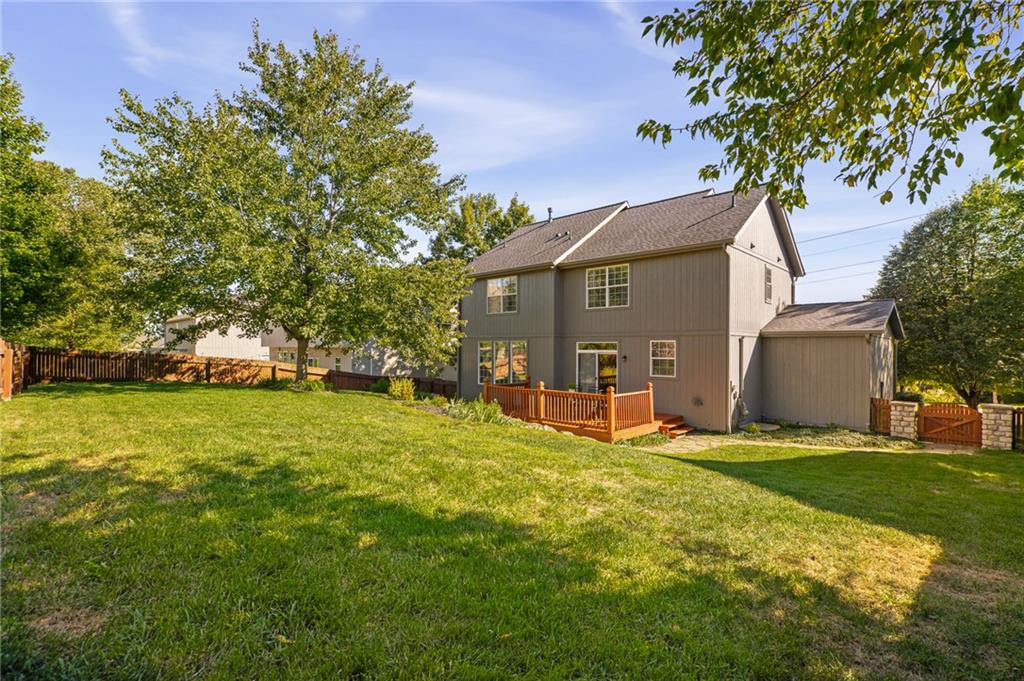 Two-story gray house with a raised deck and attached garage beyond a broad, fenced lawn.