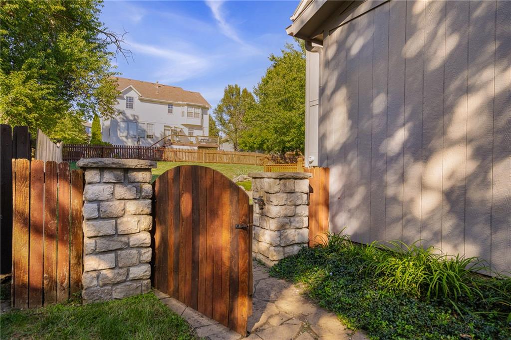 Landscaped side yard with an open wooden gate between stone pillars and a wooden fence.