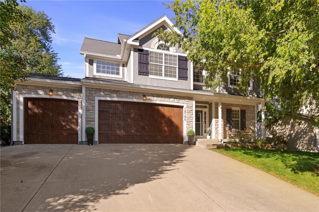 Two-story home with stone accents, three garage doors, a covered porch, and a broad driveway.