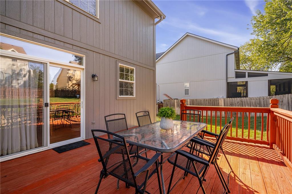 Furnished wooden deck with an outdoor dining set beside sliding glass doors and a fenced yard.