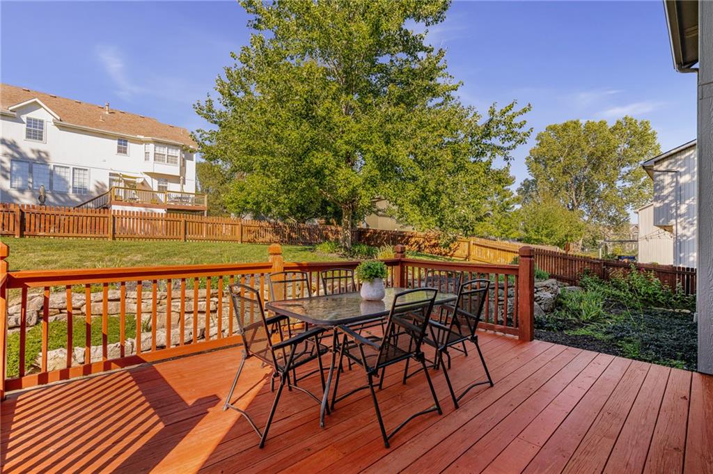 Red backyard deck with patio table and chairs overlooking a fenced lawn and mature trees.
