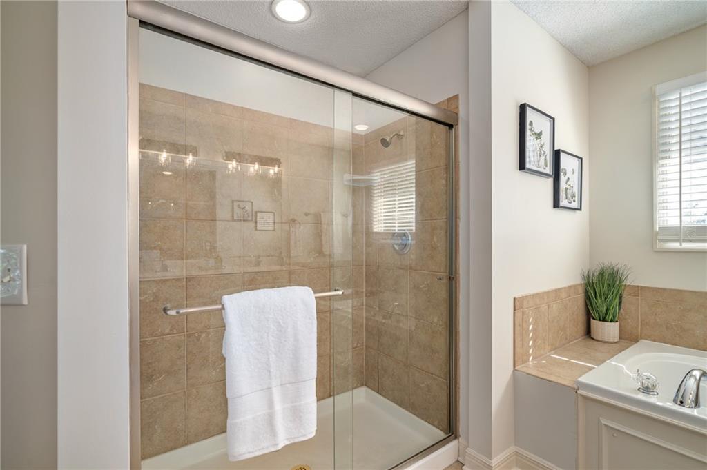 Bathroom with a glass shower, tan tile, and a corner bathtub beside a window.
