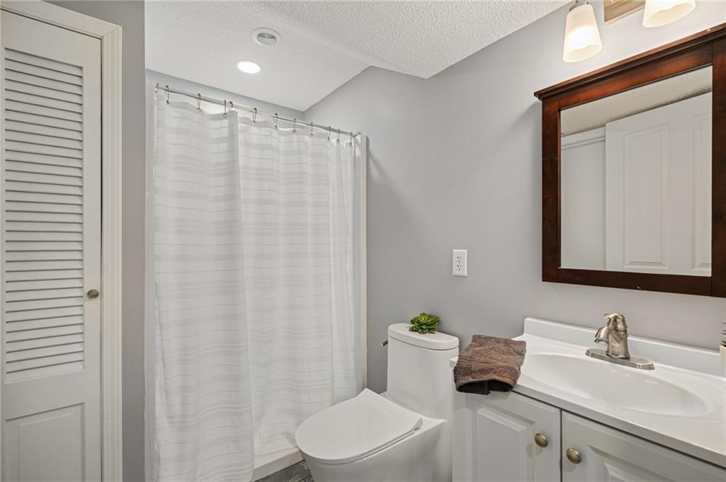 Bathroom with a white shower curtain, toilet, and vanity beneath a dark wood-framed mirror.