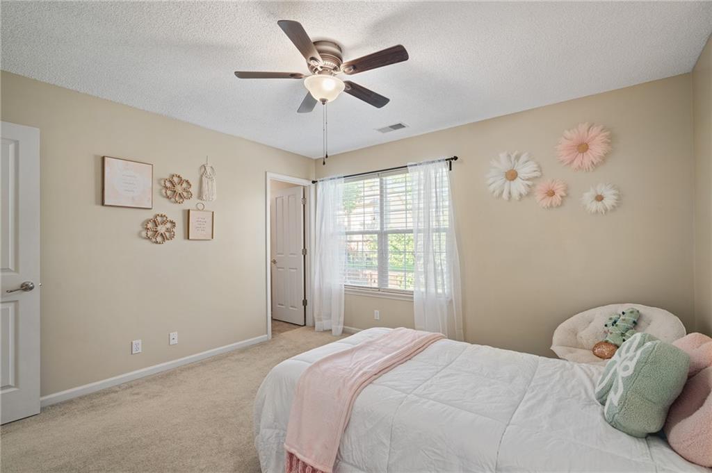 Bedroom with a white bed, pale pink throw, ceiling fan, and sheer-curtained window.