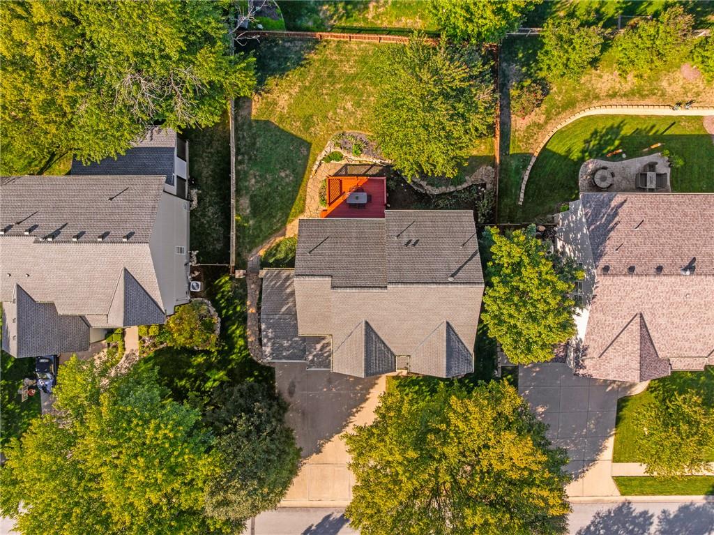 Aerial view of a home with a red backyard deck, curved stone path, and mature trees.