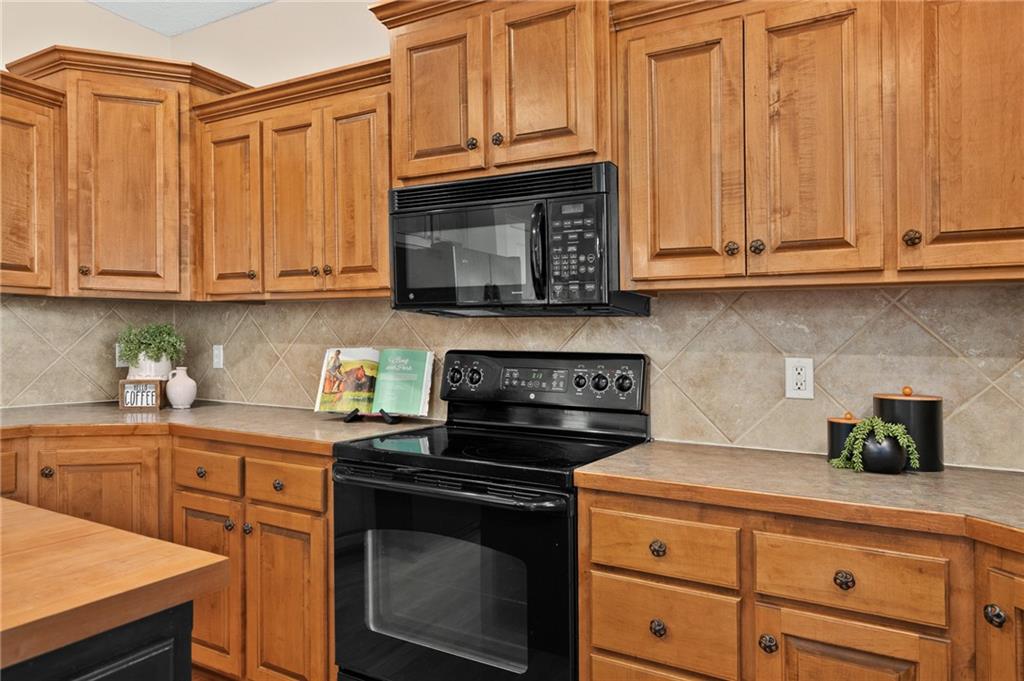Kitchen with warm wood cabinets, tiled backsplash, and black microwave and range.