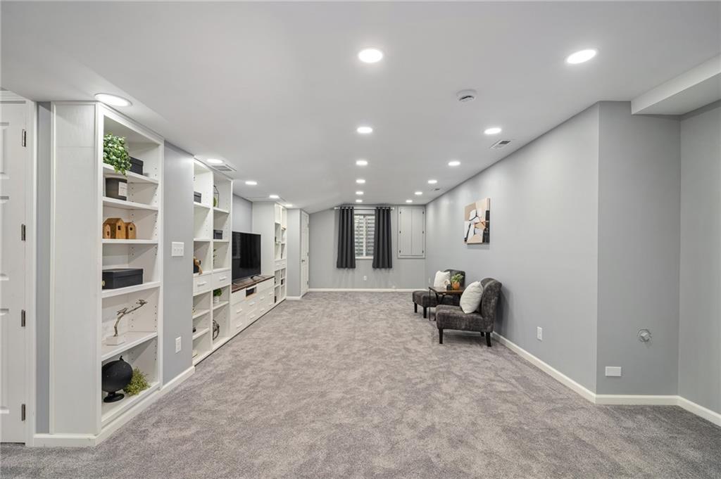 Finished basement family room with built-in shelving, gray carpet, and a small seating area.