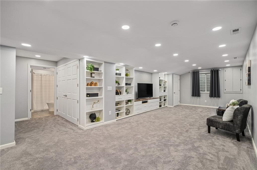 Finished basement family room with white built-ins, gray carpet, and a seating area by the window.