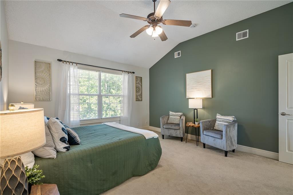 Bedroom with green bedding, a dark green accent wall, two armchairs, and a large window.