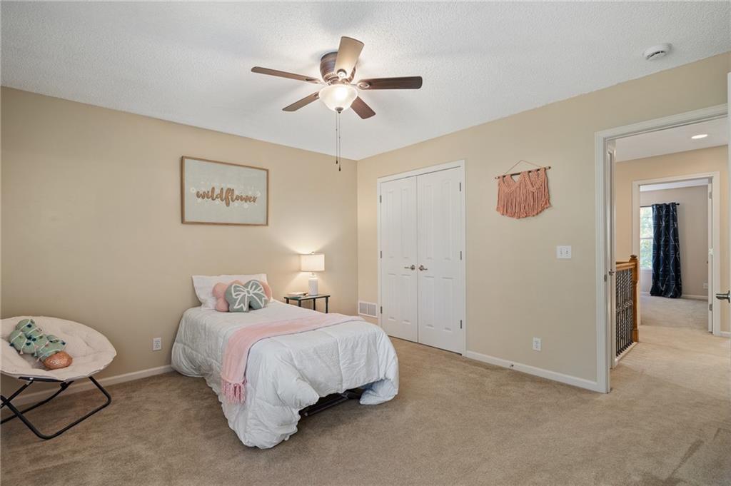 Furnished bedroom with a white bed, pink accents, beige carpet, and a ceiling fan.