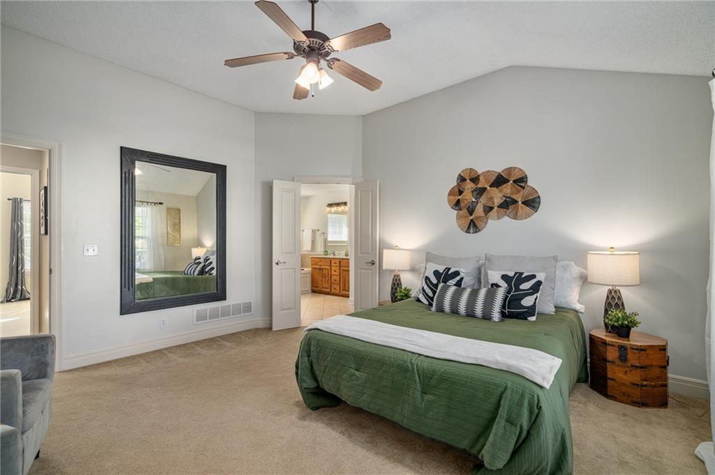 Bedroom with a green-covered bed, ceiling fan, and open doorway to the bathroom.