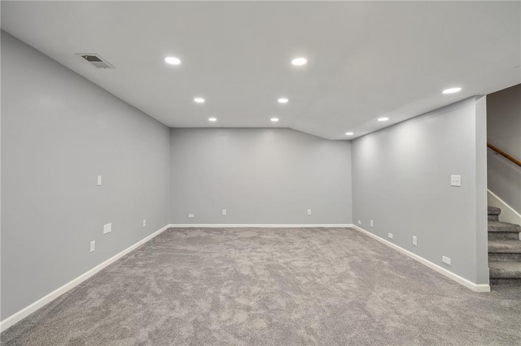 Empty basement room with gray carpeting and recessed lights, next to a staircase.