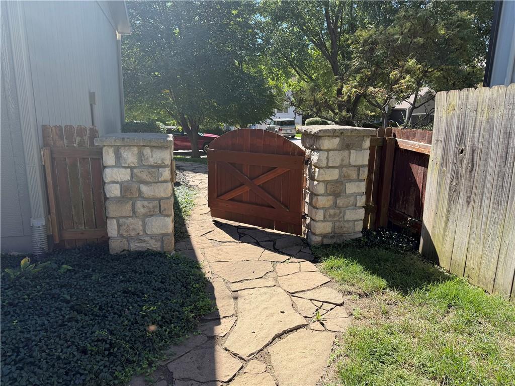 Stone walkway leading through an open wooden gate between stone pillars and wooden fences.