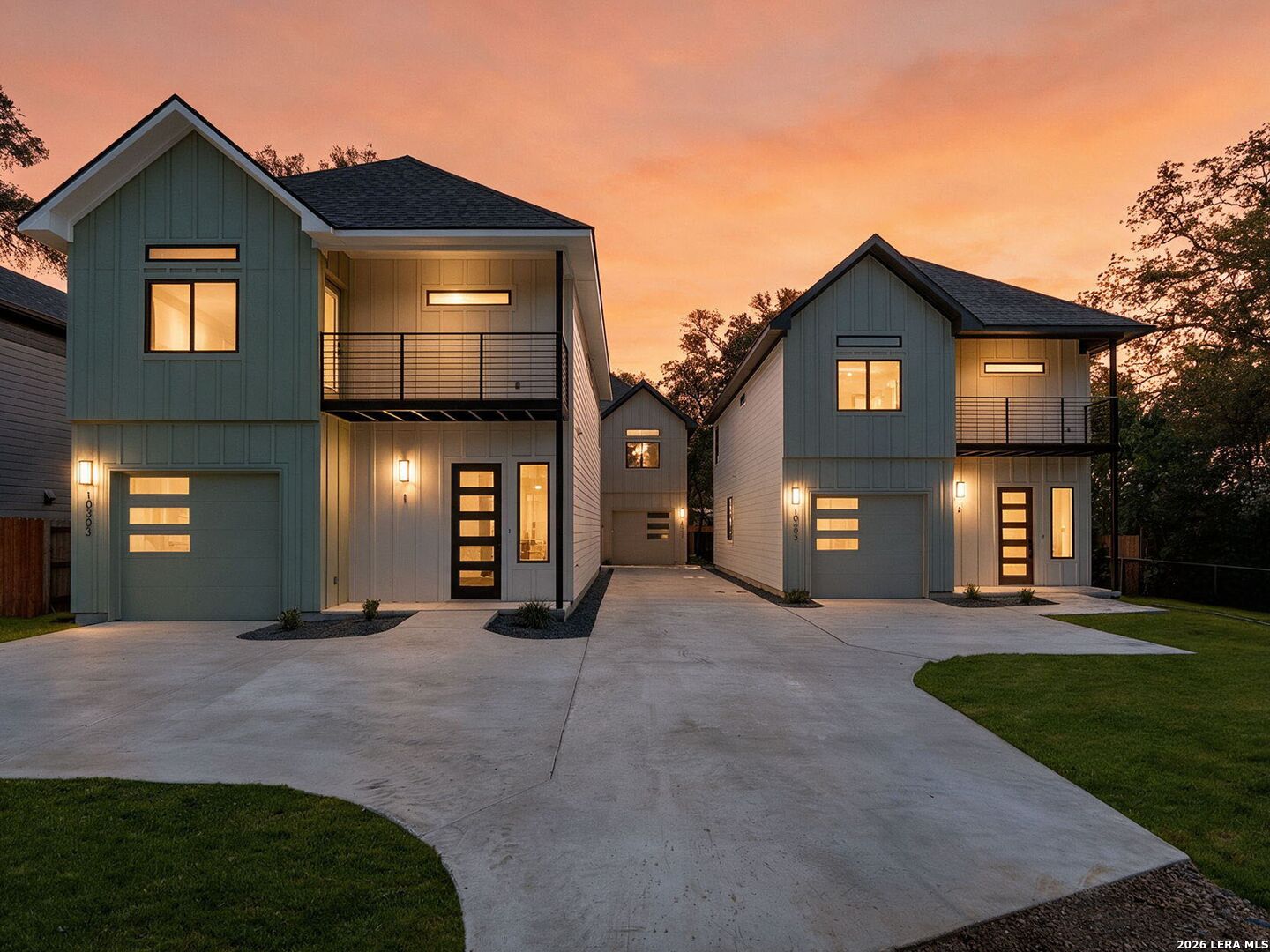Modern two-story homes with garages and balconies glow beneath a sunset sky.