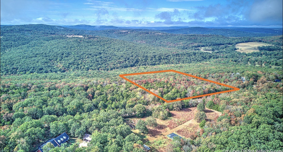 Aerial view of a wooded parcel outlined in orange, with forest and distant hills beyond.