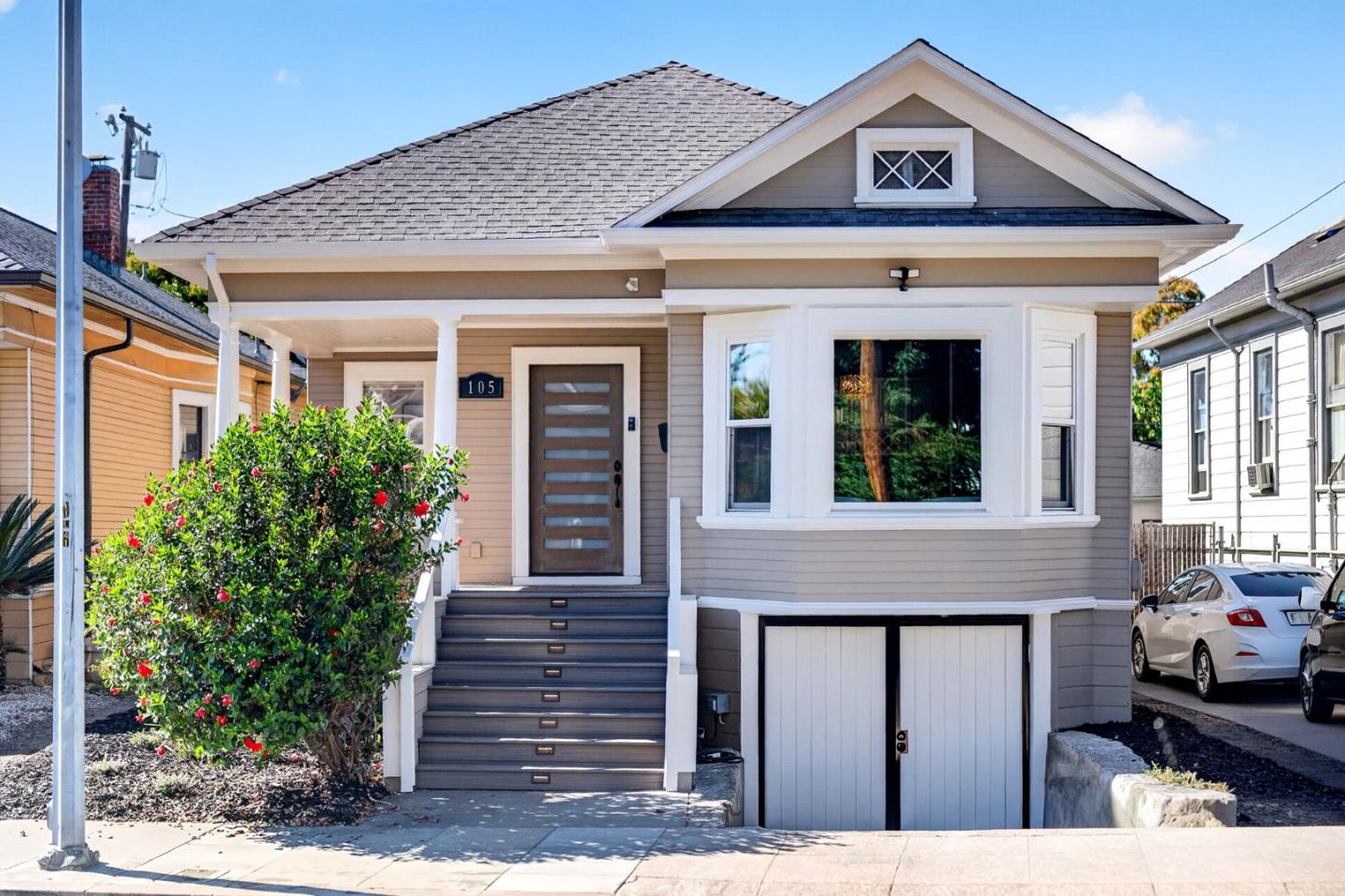 Raised gray house with white trim, front steps, and a garage beneath the house.