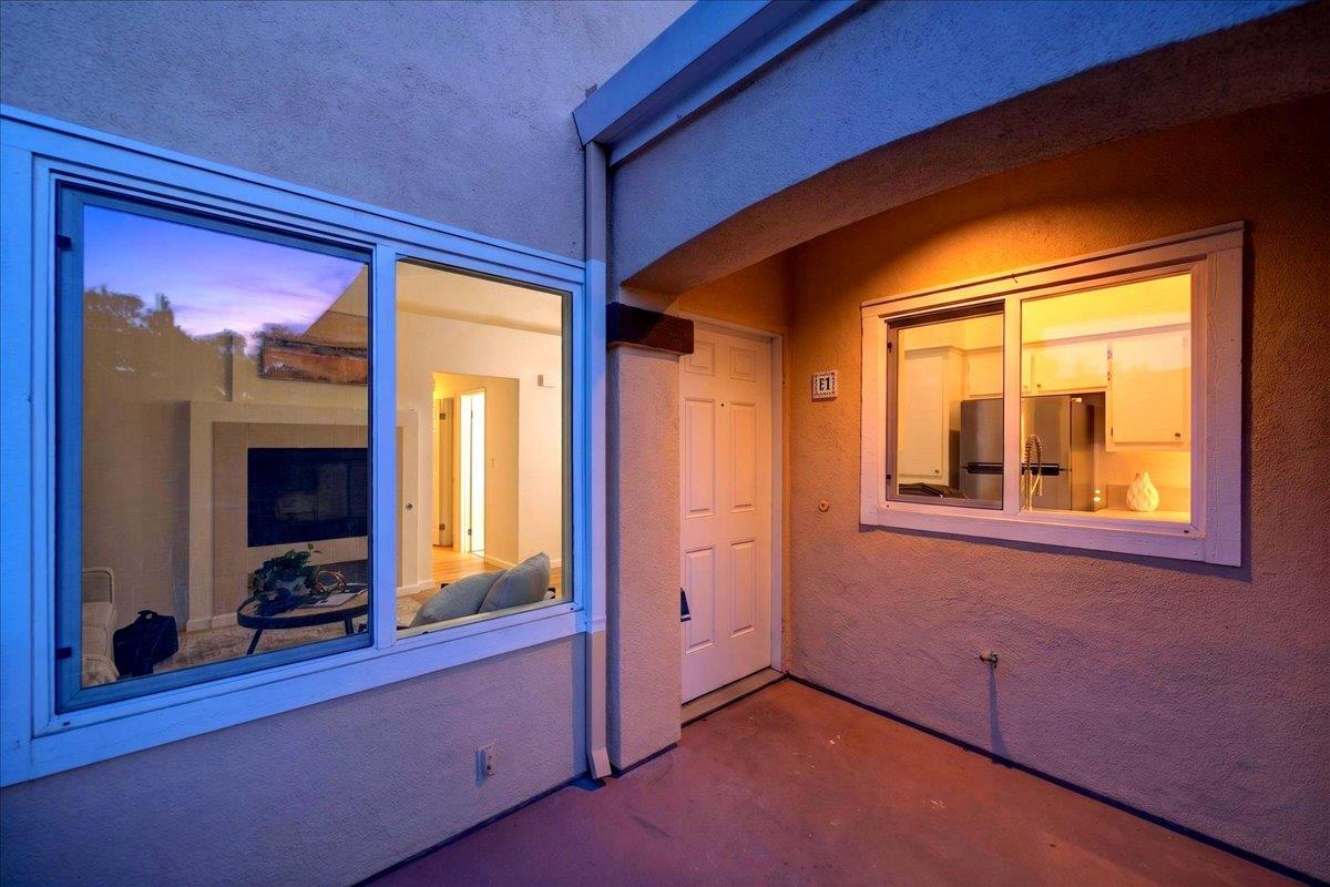 Covered patio at dusk with windows looking into a warmly lit living room and kitchen.