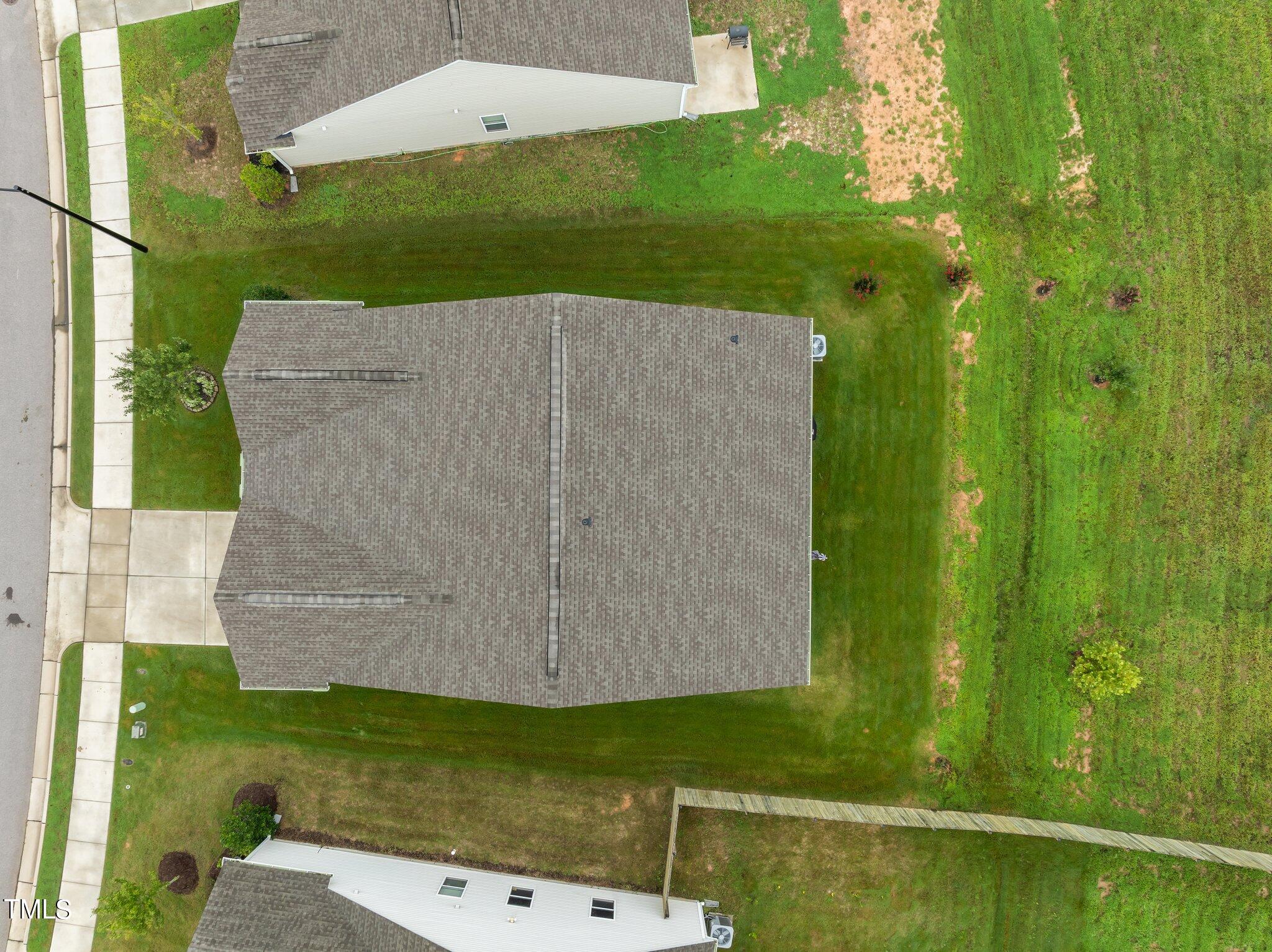Aerial view of a home with a large gray shingle roof and lawn beside the sidewalk.