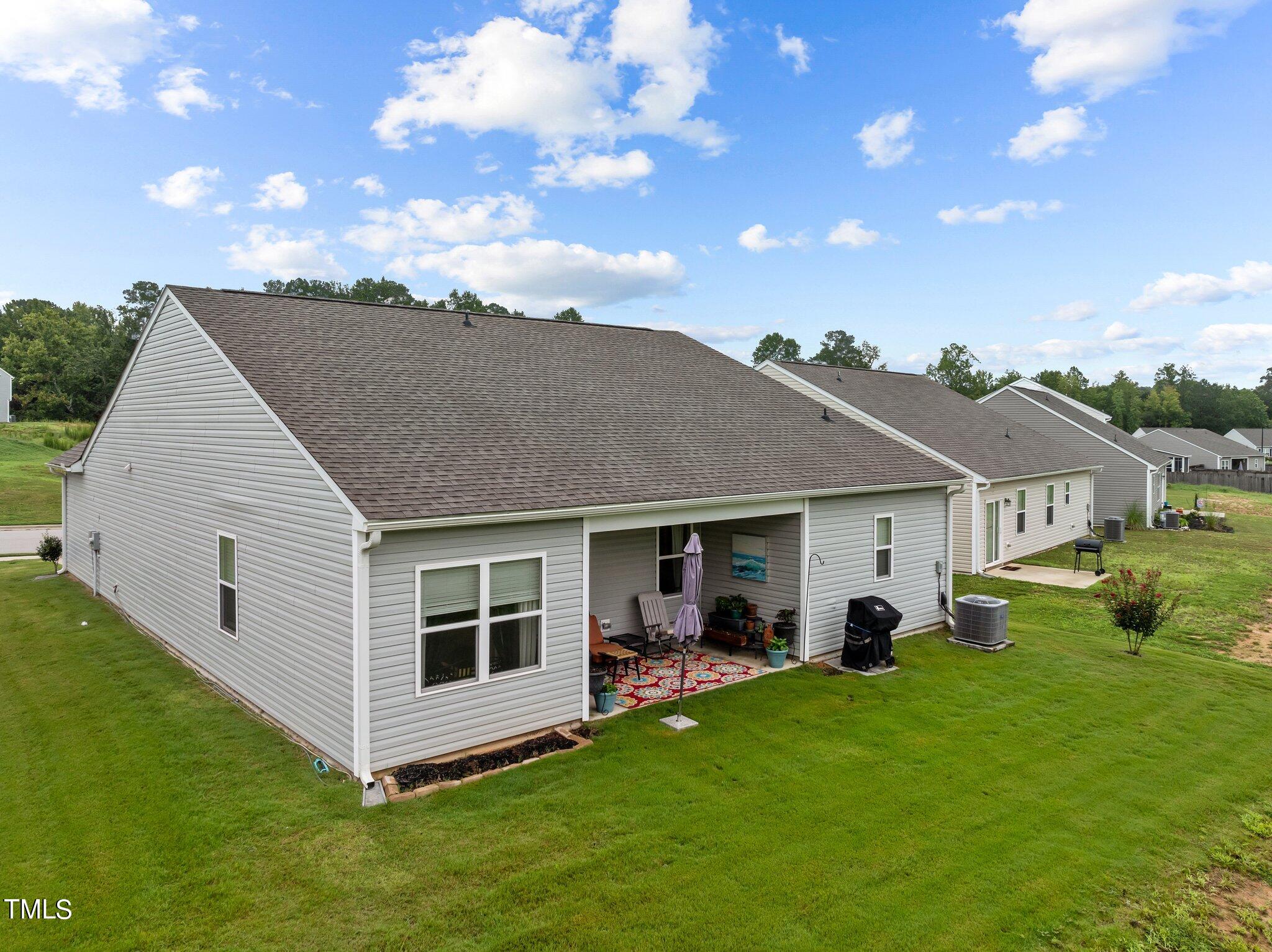Rear exterior of a gray-sided home with a covered patio and broad lawn.