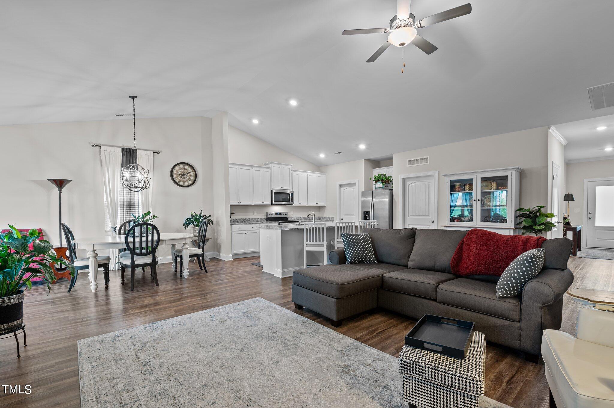 Open-plan living room, dining area, and kitchen with a dark sectional, white cabinetry, and wood floors.